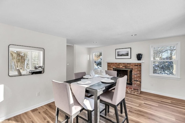 dining space with a brick fireplace, light hardwood / wood-style floors, and a wealth of natural light