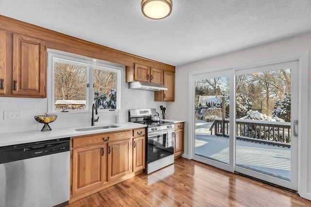 kitchen featuring appliances with stainless steel finishes, a textured ceiling, decorative backsplash, sink, and light hardwood / wood-style flooring