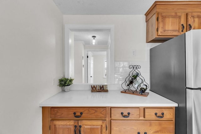 kitchen with backsplash, a textured ceiling, and stainless steel fridge