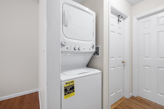 laundry area featuring laundry area, stacked washer and dryer, light wood-style flooring, and baseboards