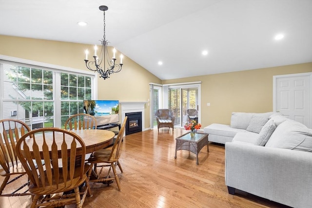 dining area featuring a notable chandelier, a glass covered fireplace, recessed lighting, light wood finished floors, and lofted ceiling