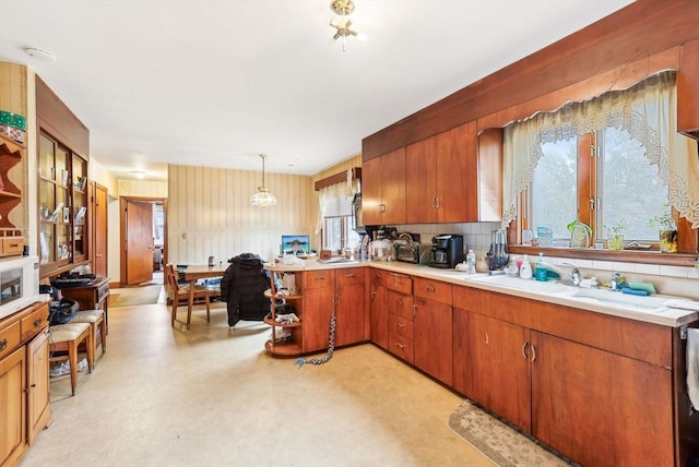 kitchen with a sink, light countertops, hanging light fixtures, decorative backsplash, and light floors