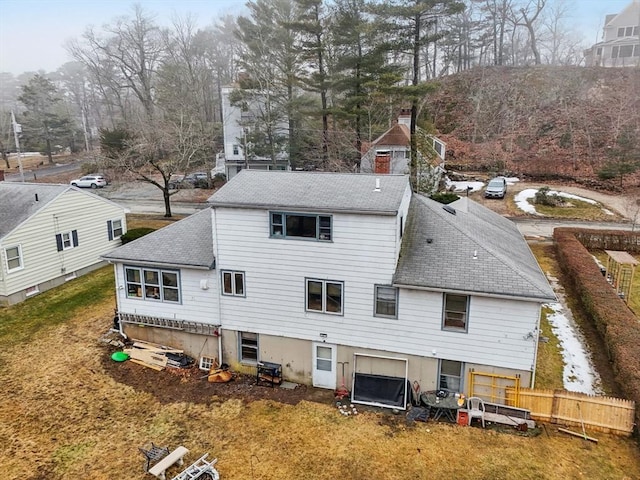 back of house featuring a chimney, fence, and roof with shingles