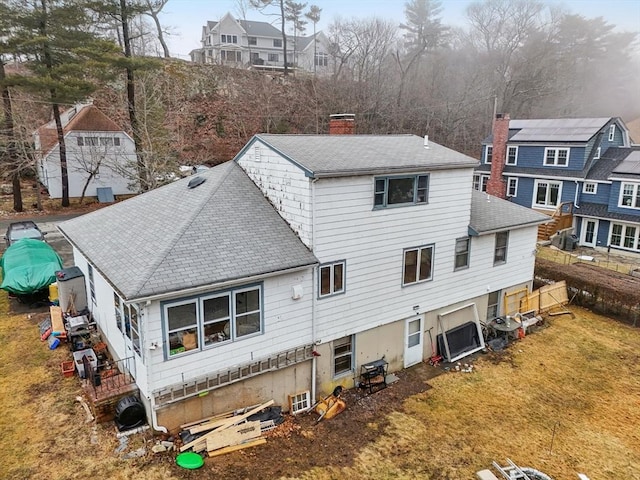 back of property featuring a lawn, a shingled roof, a chimney, and a residential view