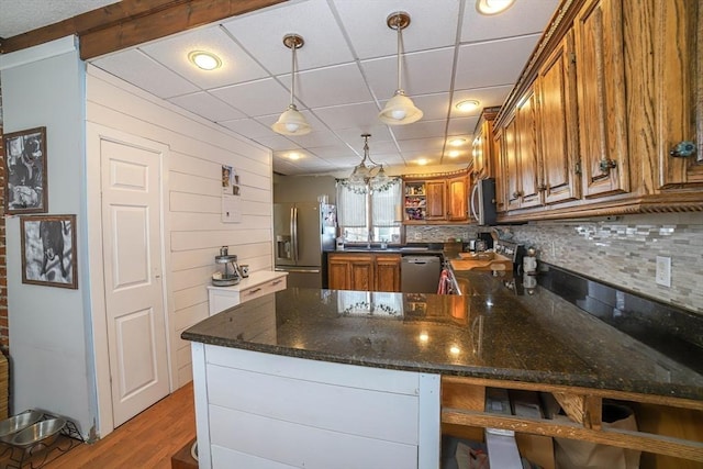 kitchen featuring dark stone countertops, backsplash, stainless steel appliances, decorative light fixtures, and kitchen peninsula