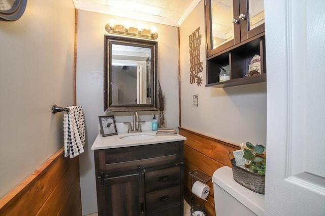 bathroom with crown molding, vanity, toilet, and wood walls