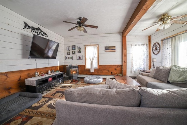 living room featuring ceiling fan, wooden walls, a wood stove, and beam ceiling