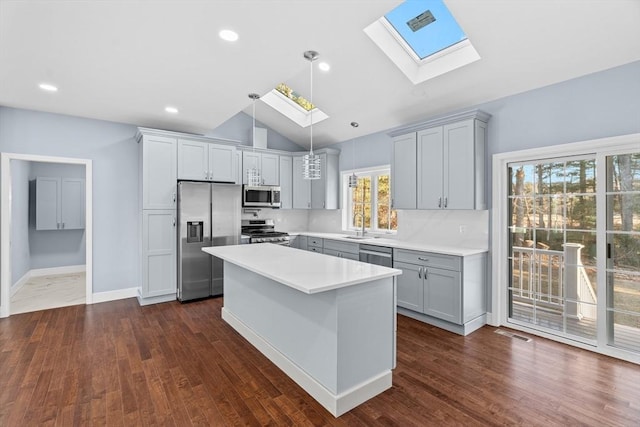 kitchen with pendant lighting, a center island, vaulted ceiling with skylight, appliances with stainless steel finishes, and a healthy amount of sunlight