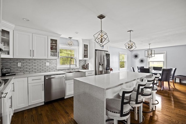 kitchen with decorative backsplash, white cabinets, a sink, stainless steel appliances, and hanging light fixtures