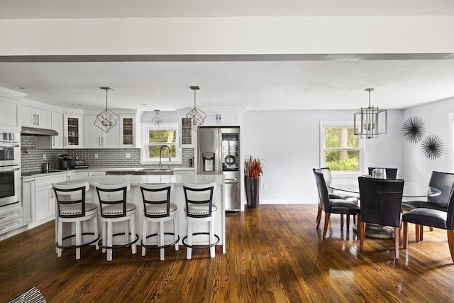 kitchen with tasteful backsplash, white cabinets, glass insert cabinets, appliances with stainless steel finishes, and under cabinet range hood