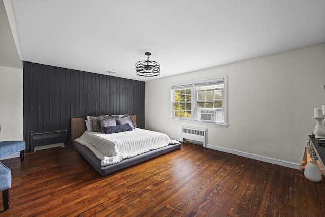 bedroom featuring wood finished floors, cooling unit, radiator heating unit, baseboards, and visible vents