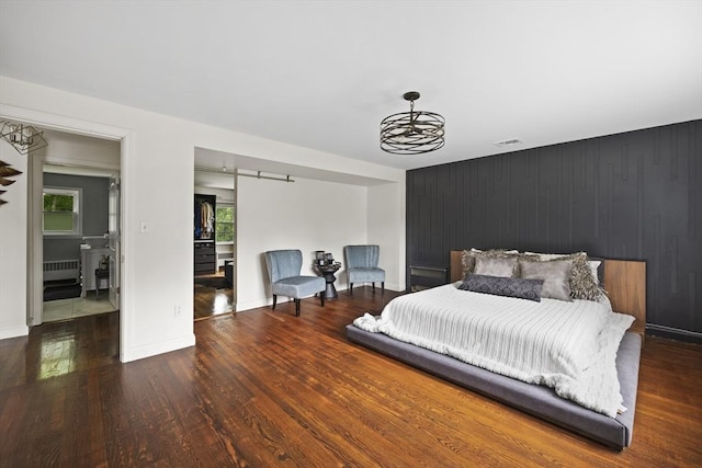 bedroom with wood finished floors, a barn door, radiator heating unit, baseboards, and visible vents