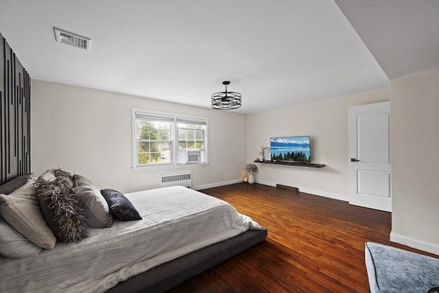 bedroom featuring visible vents, radiator, a notable chandelier, and wood finished floors
