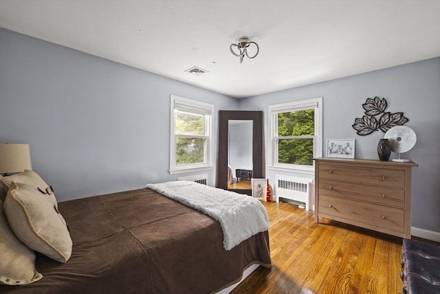 bedroom with radiator heating unit, wood finished floors, and visible vents