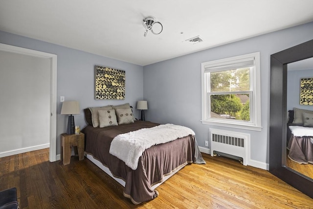 bedroom featuring visible vents, radiator heating unit, wood finished floors, and baseboards