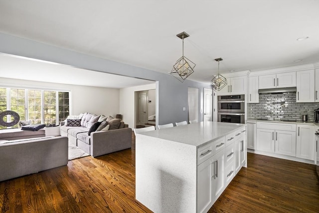 kitchen with double oven, tasteful backsplash, white cabinets, open floor plan, and dark wood finished floors