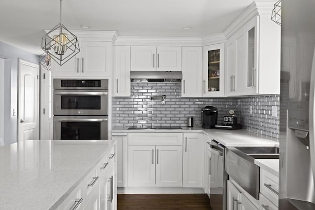kitchen with white cabinetry, glass insert cabinets, a chandelier, stainless steel appliances, and under cabinet range hood