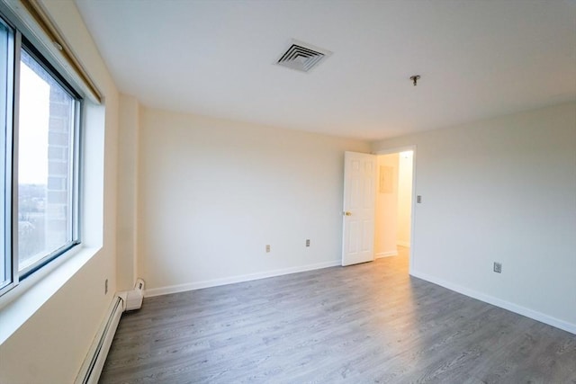 empty room with a wealth of natural light, dark wood-type flooring, and a baseboard radiator