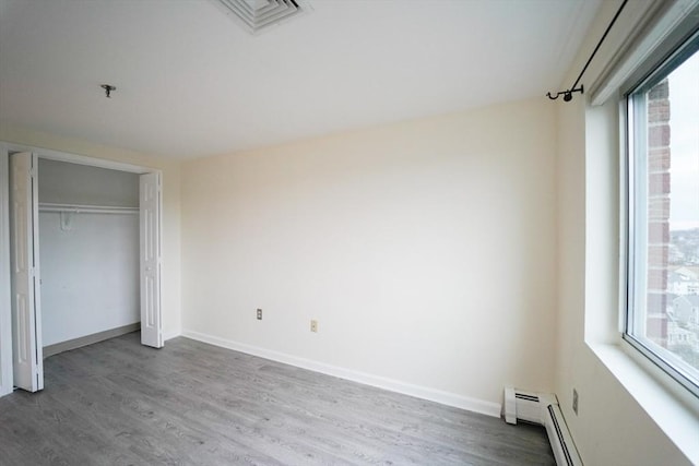 unfurnished bedroom with hardwood / wood-style flooring and a baseboard heating unit