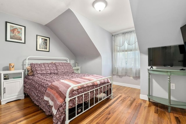 bedroom with baseboards, lofted ceiling, and hardwood / wood-style flooring