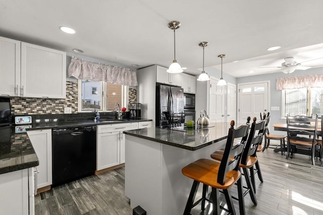 kitchen with wood finished floors, backsplash, black appliances, and a breakfast bar