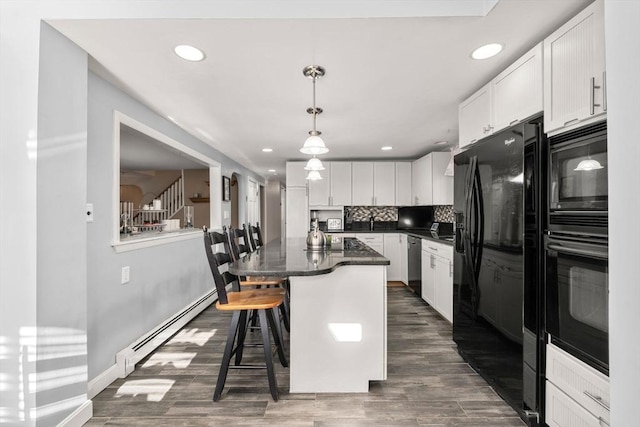 kitchen with tasteful backsplash, a kitchen bar, baseboard heating, white cabinets, and black appliances