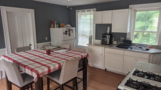 kitchen with white appliances, hardwood / wood-style flooring, white cabinetry, and sink