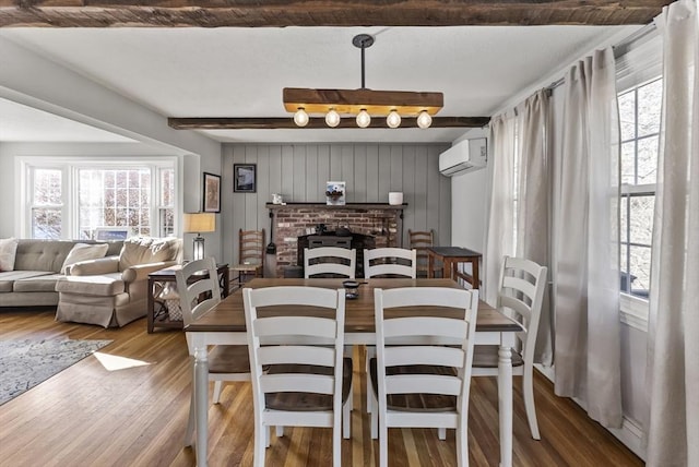 dining room with a wall mounted air conditioner, a fireplace, wood-type flooring, and beam ceiling