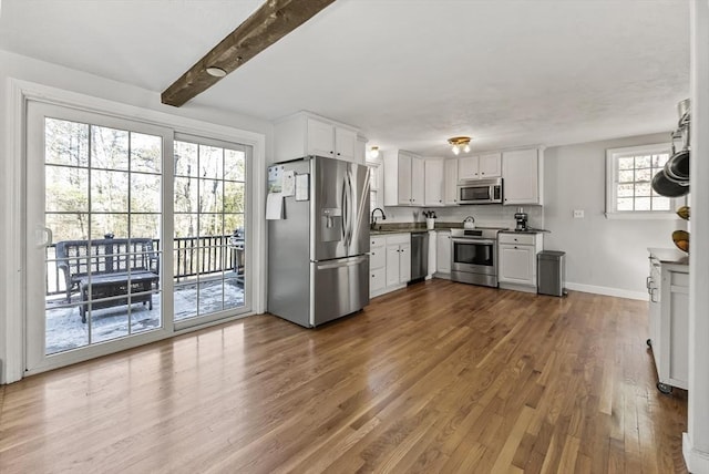 kitchen featuring sink, appliances with stainless steel finishes, white cabinetry, wood-type flooring, and beamed ceiling