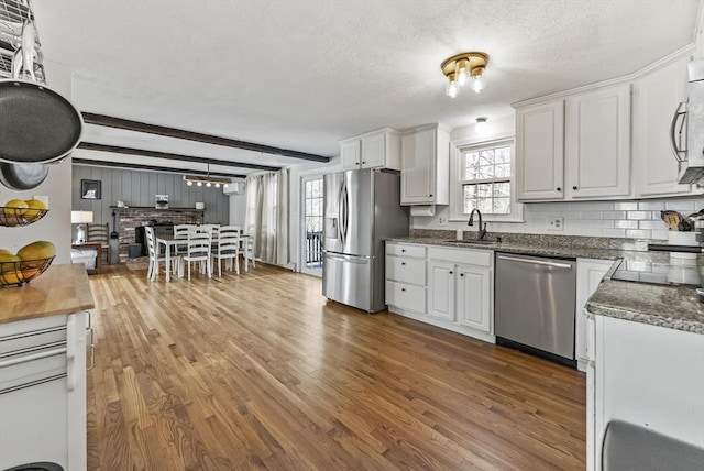 kitchen with appliances with stainless steel finishes, sink, white cabinets, plenty of natural light, and beam ceiling