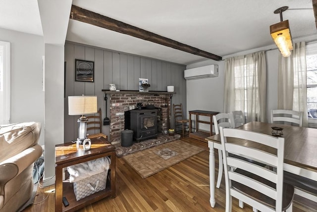 living room with wooden walls, a wood stove, a wall mounted AC, hardwood / wood-style flooring, and beam ceiling