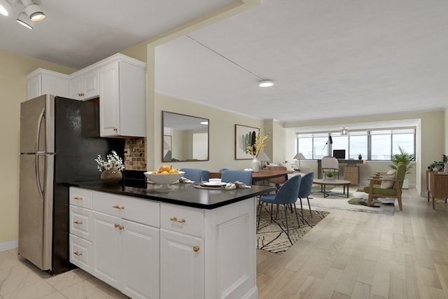 kitchen with white cabinets, backsplash, light hardwood / wood-style floors, and stainless steel refrigerator