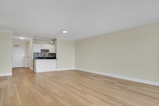 unfurnished living room featuring ornamental molding, sink, and light hardwood / wood-style floors