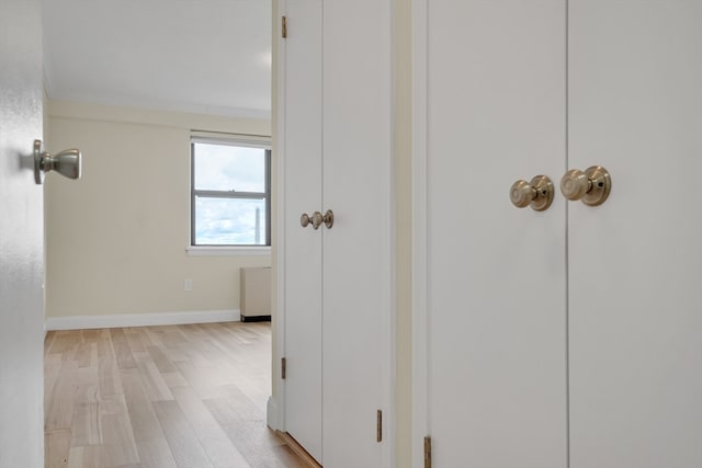 hallway with light wood-type flooring and crown molding