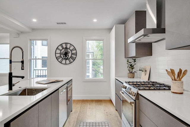 kitchen featuring wall chimney range hood, stainless steel appliances, a sink, plenty of natural light, and recessed lighting