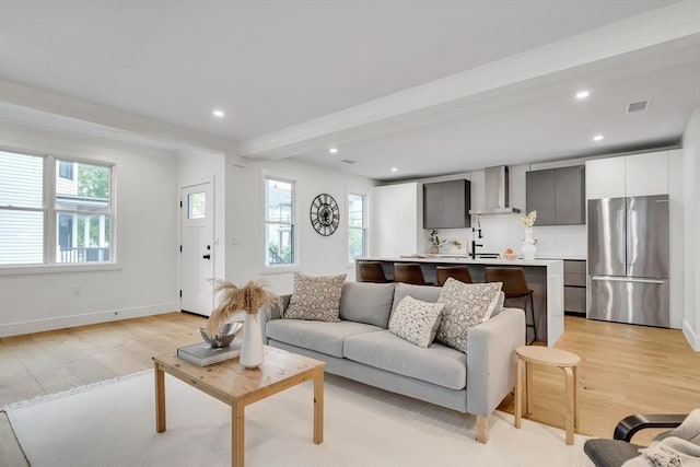living area with light wood-style flooring, beamed ceiling, recessed lighting, and baseboards