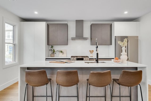 kitchen featuring wall chimney exhaust hood, a kitchen bar, light wood-style floors, stainless steel appliances, and light countertops
