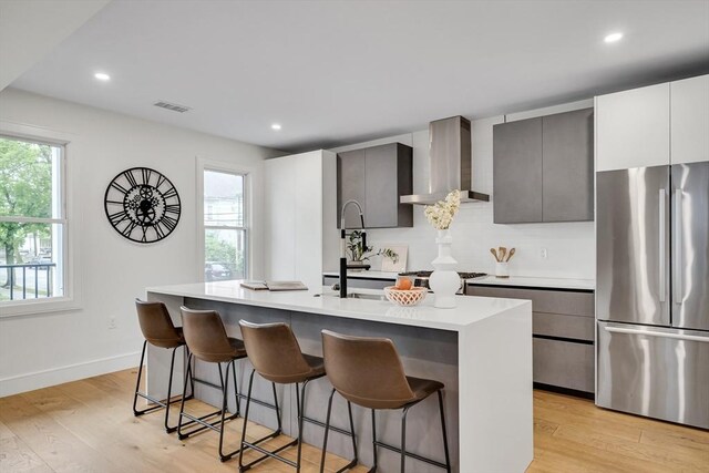kitchen with freestanding refrigerator, wall chimney range hood, a breakfast bar area, light countertops, and recessed lighting