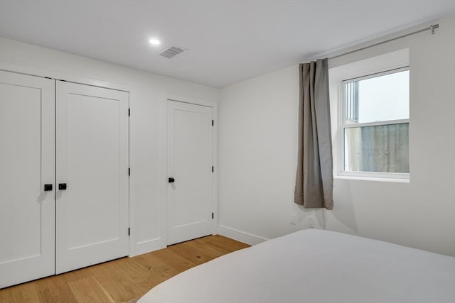 bedroom with light wood-style floors, multiple closets, baseboards, and recessed lighting