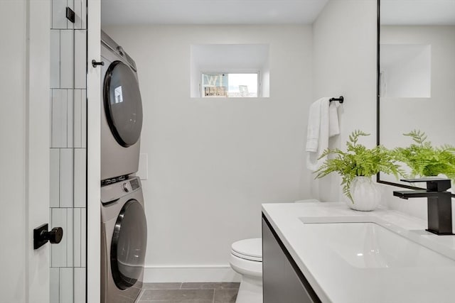 bathroom with estacked washer and dryer, toilet, vanity, and baseboards