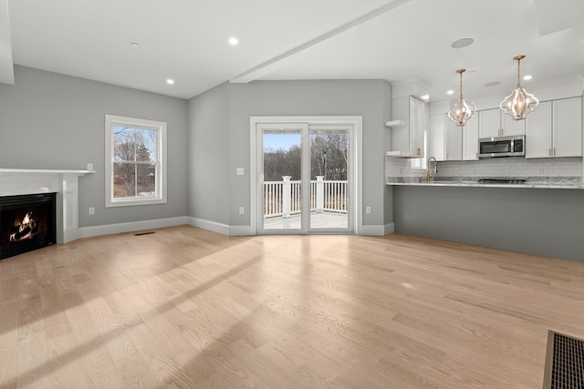 unfurnished living room featuring light wood-type flooring, sink, and plenty of natural light