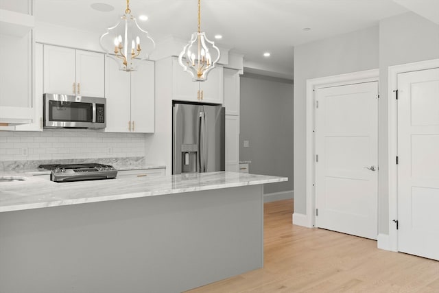 kitchen with kitchen peninsula, white cabinets, hanging light fixtures, light hardwood / wood-style flooring, and stainless steel appliances