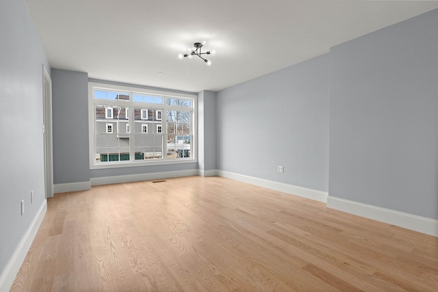 empty room featuring a notable chandelier and light wood-type flooring