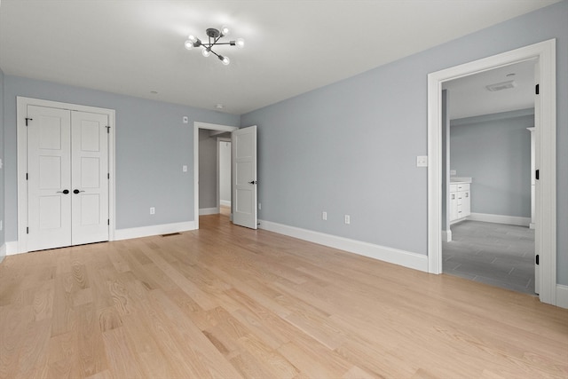 unfurnished bedroom with a closet, an inviting chandelier, and light wood-type flooring