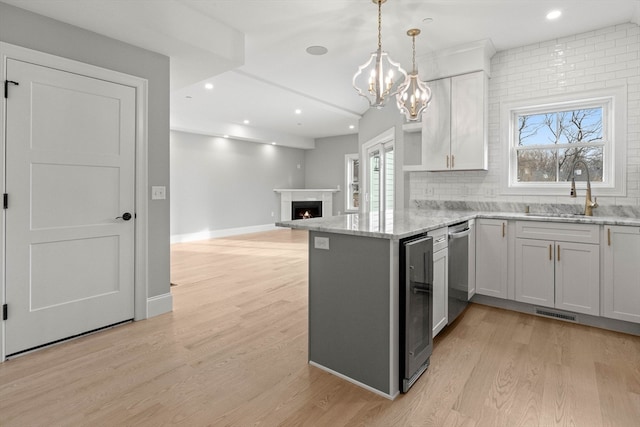 kitchen featuring kitchen peninsula, white cabinets, hanging light fixtures, light hardwood / wood-style flooring, and sink