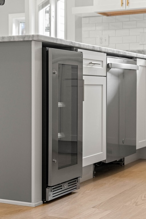 details with stainless steel dishwasher, white cabinets, light wood-type flooring, and beverage cooler