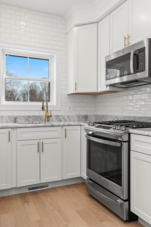 kitchen with stainless steel appliances, light stone countertops, light hardwood / wood-style flooring, and white cabinets