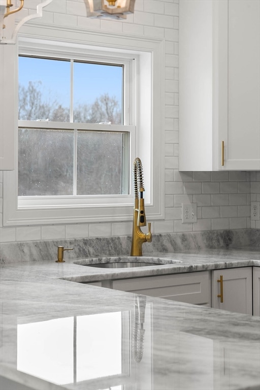 room details featuring decorative backsplash, white cabinets, sink, and light stone counters