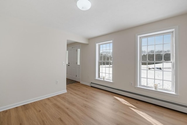 spare room with light wood finished floors, baseboard heating, and baseboards