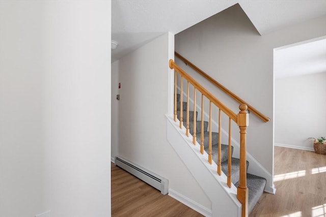 stairs with baseboards, a baseboard heating unit, and wood finished floors